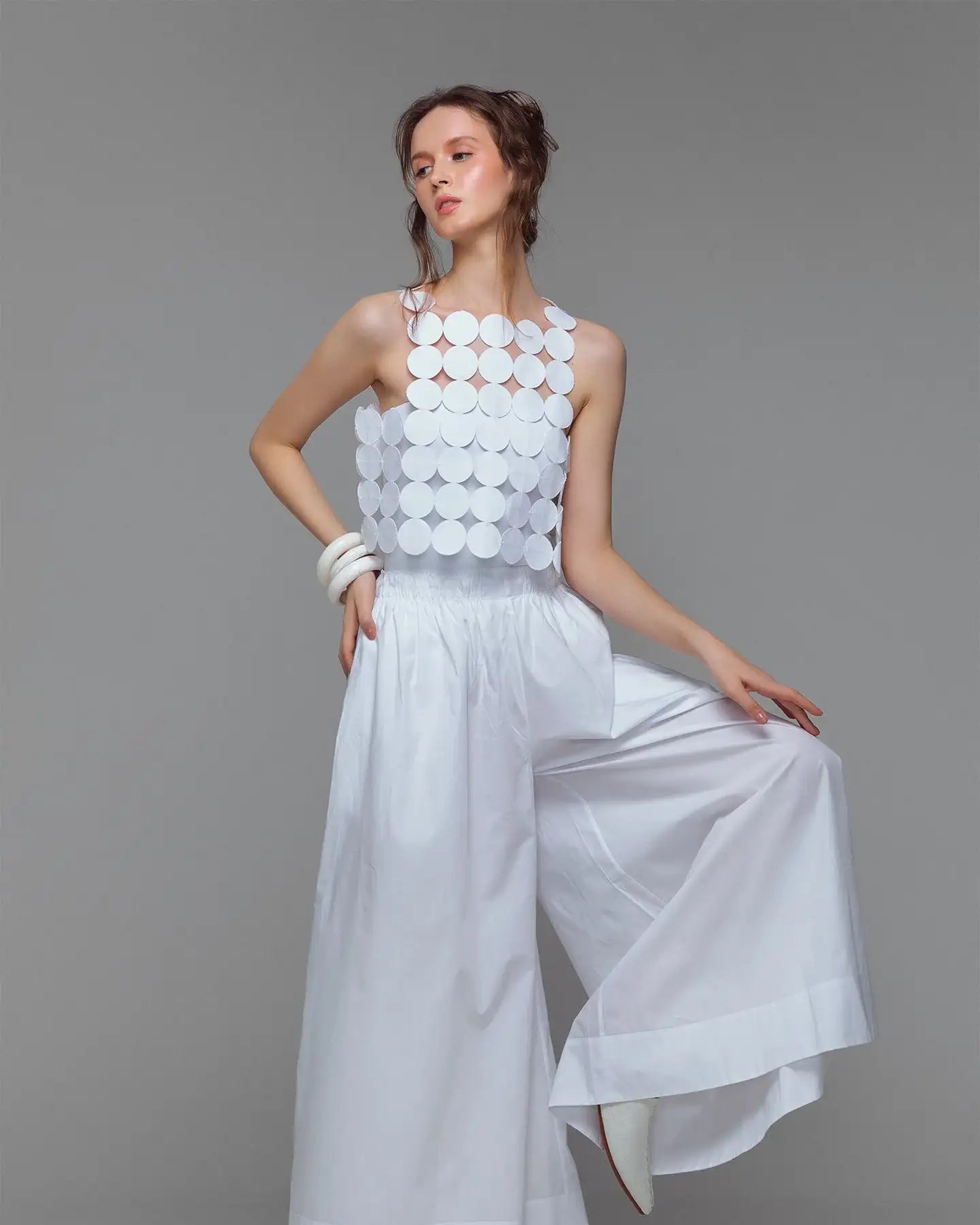 Woman modeling modern white sleeveless circular top and wide-leg trousers, minimalist fashion