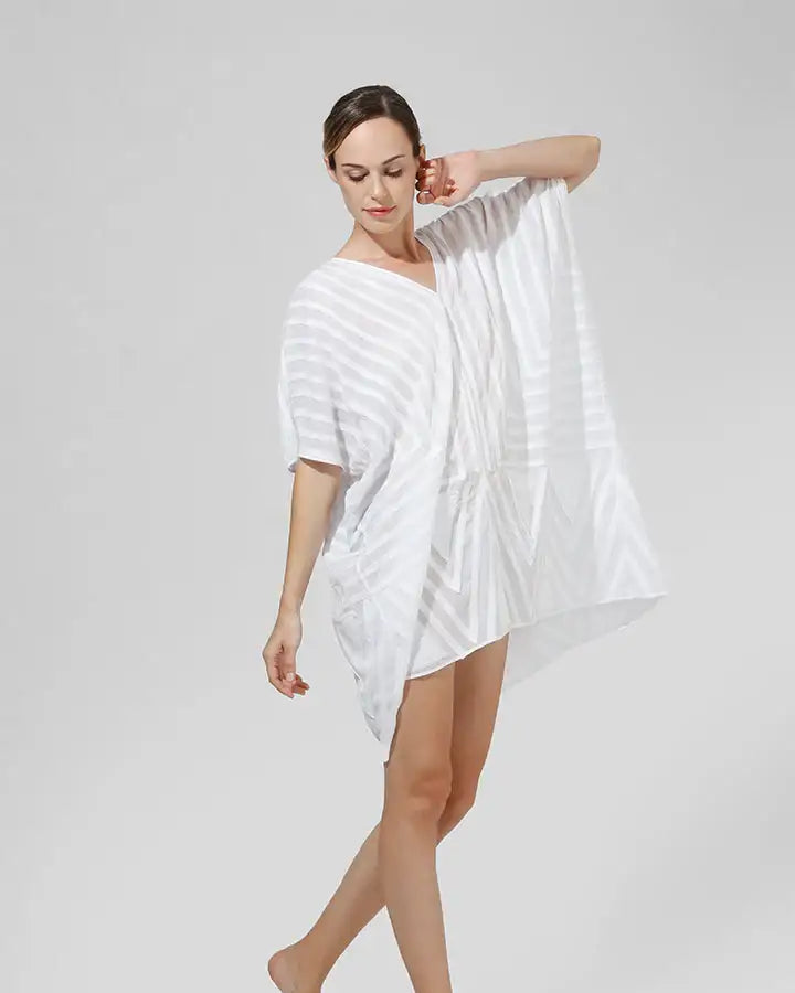 Woman modeling a loose white striped kaftan dress on a plain background