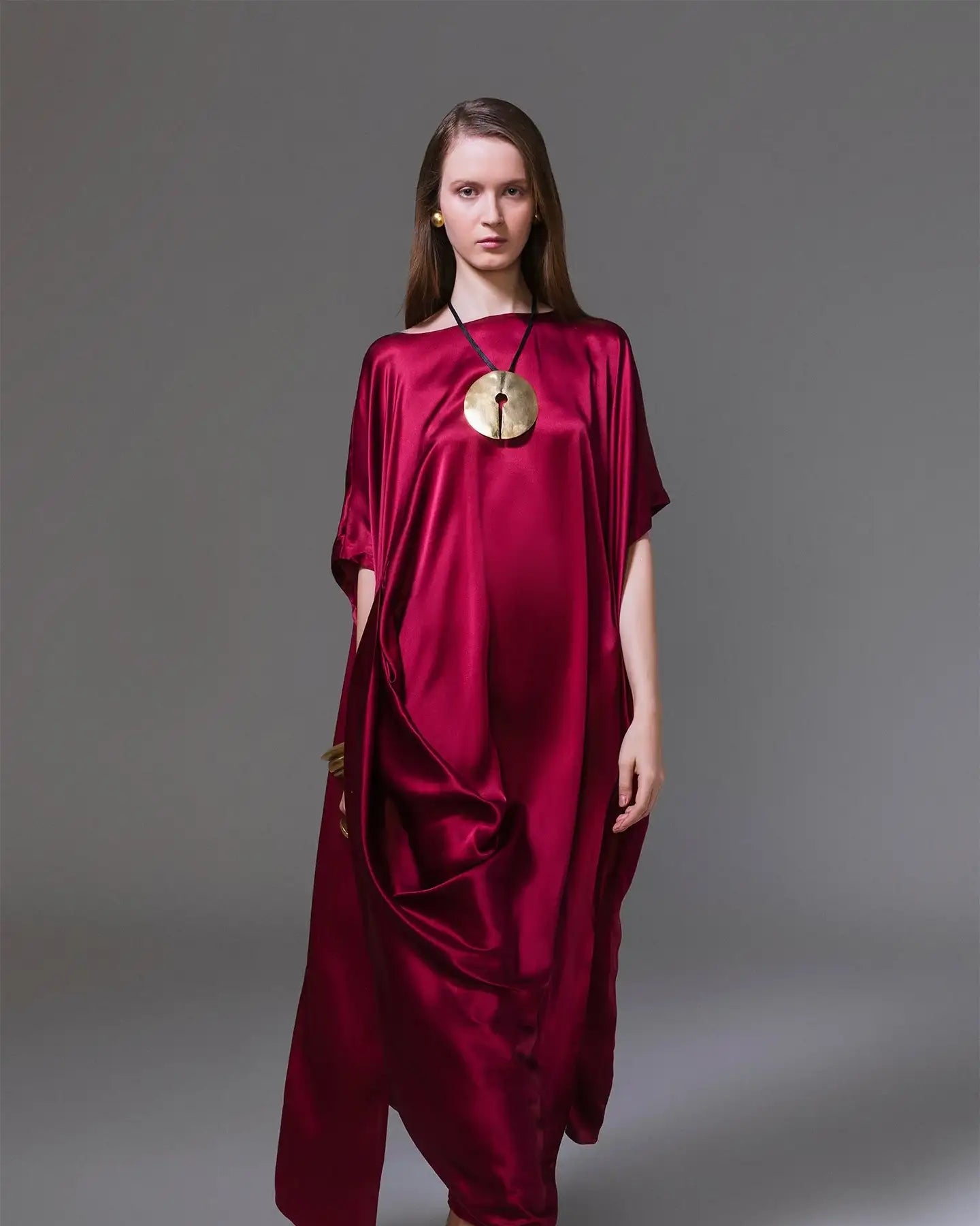 Woman wearing a flowing red satin dress, gold statement necklace, and strappy sandals