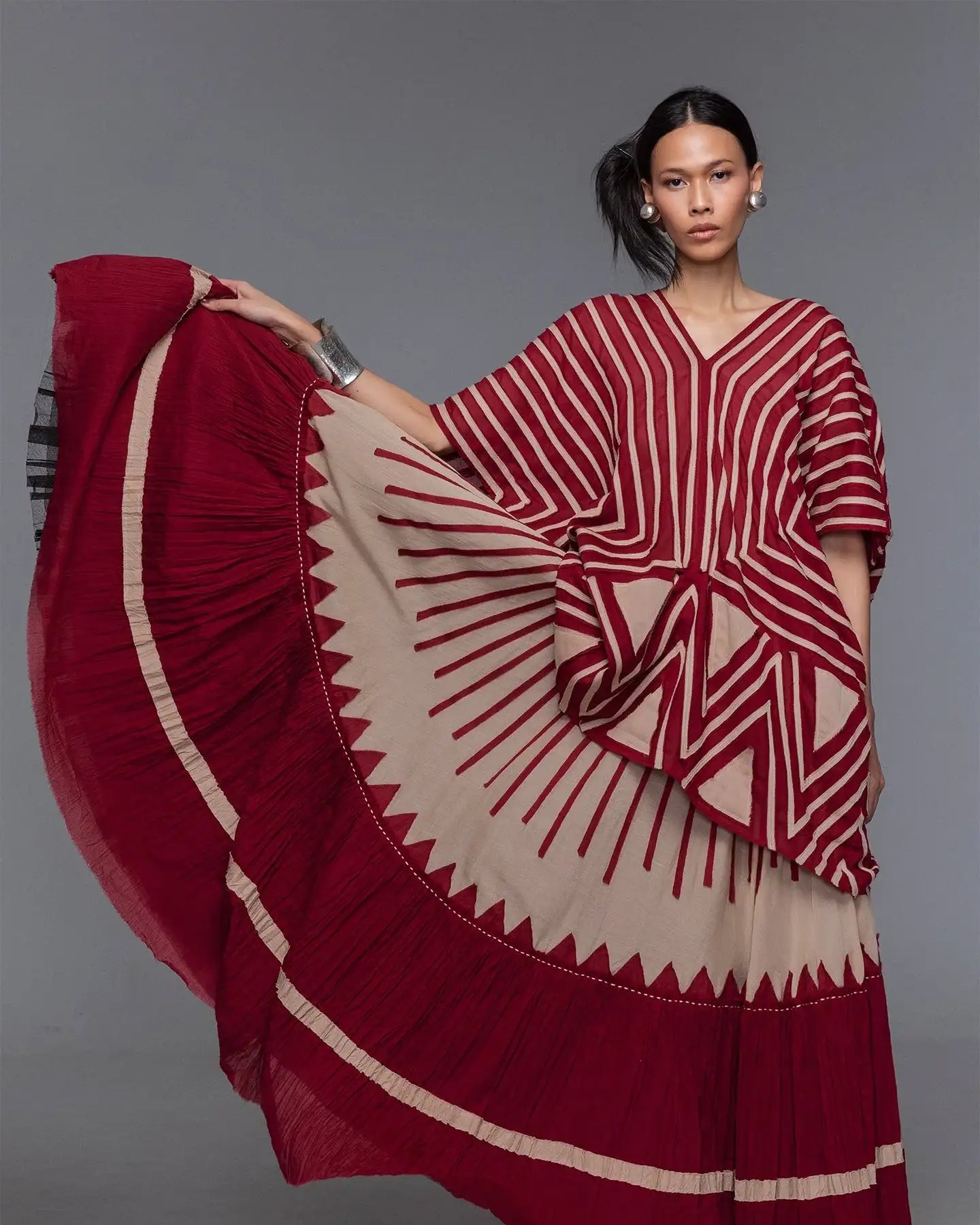Woman wearing modern red and beige geometric-patterned dress with flowy skirt, studio backdrop