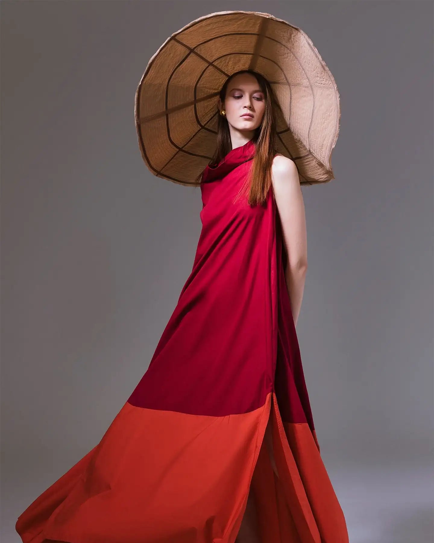 Woman in flowy two-tone red and orange maxi dress, large wide-brim hat, and yellow sandals