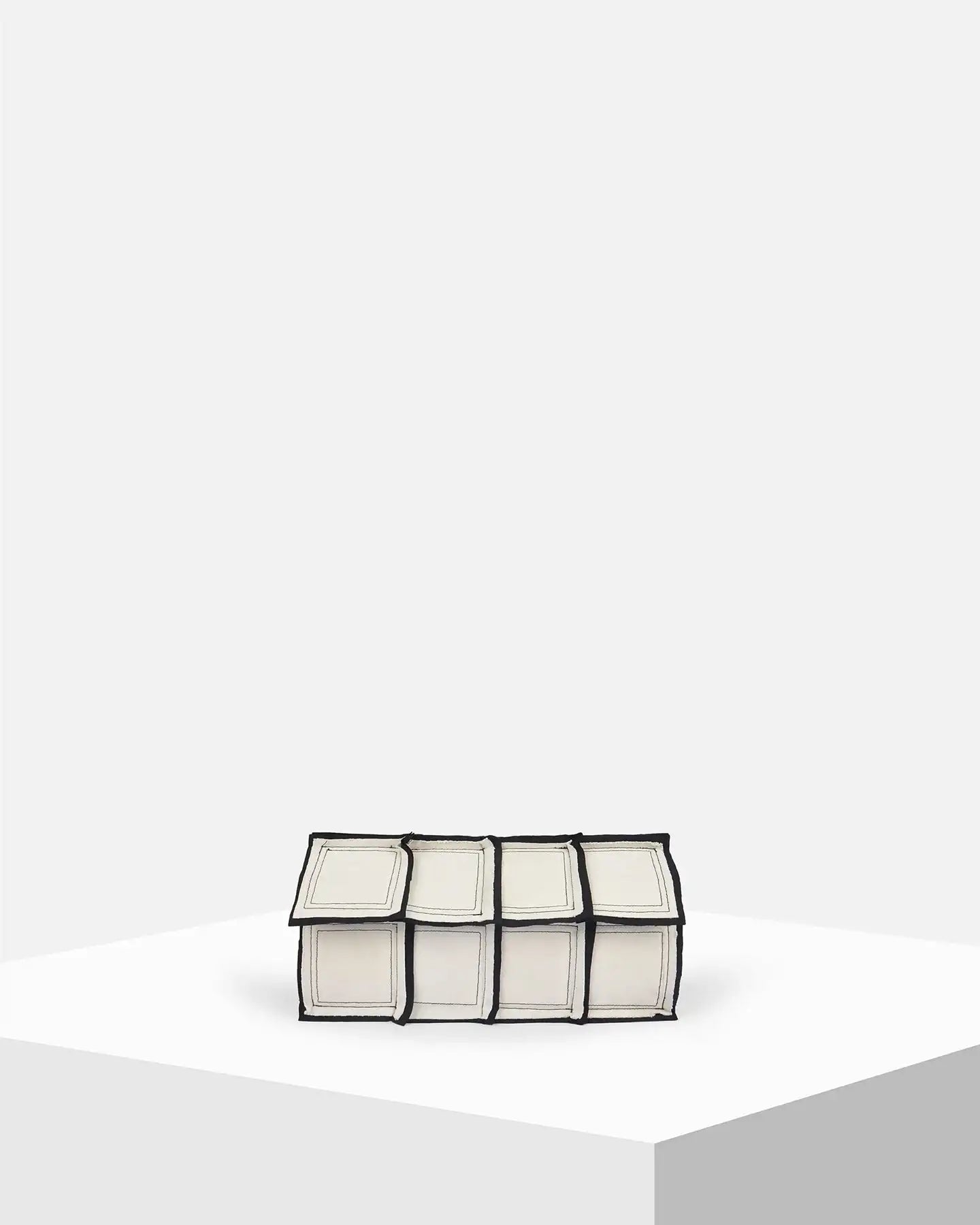 Geometric white and black clutch bag with paneled design on a minimalist display pedestal.