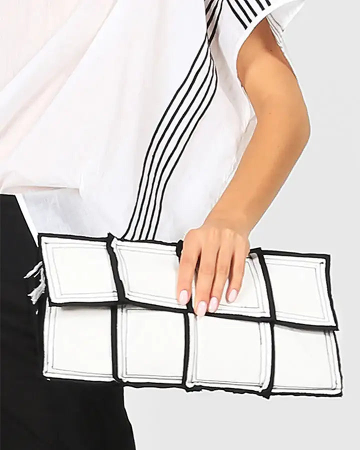 Woman holding a modern white geometric clutch bag with black trim, stylish fashion accessory