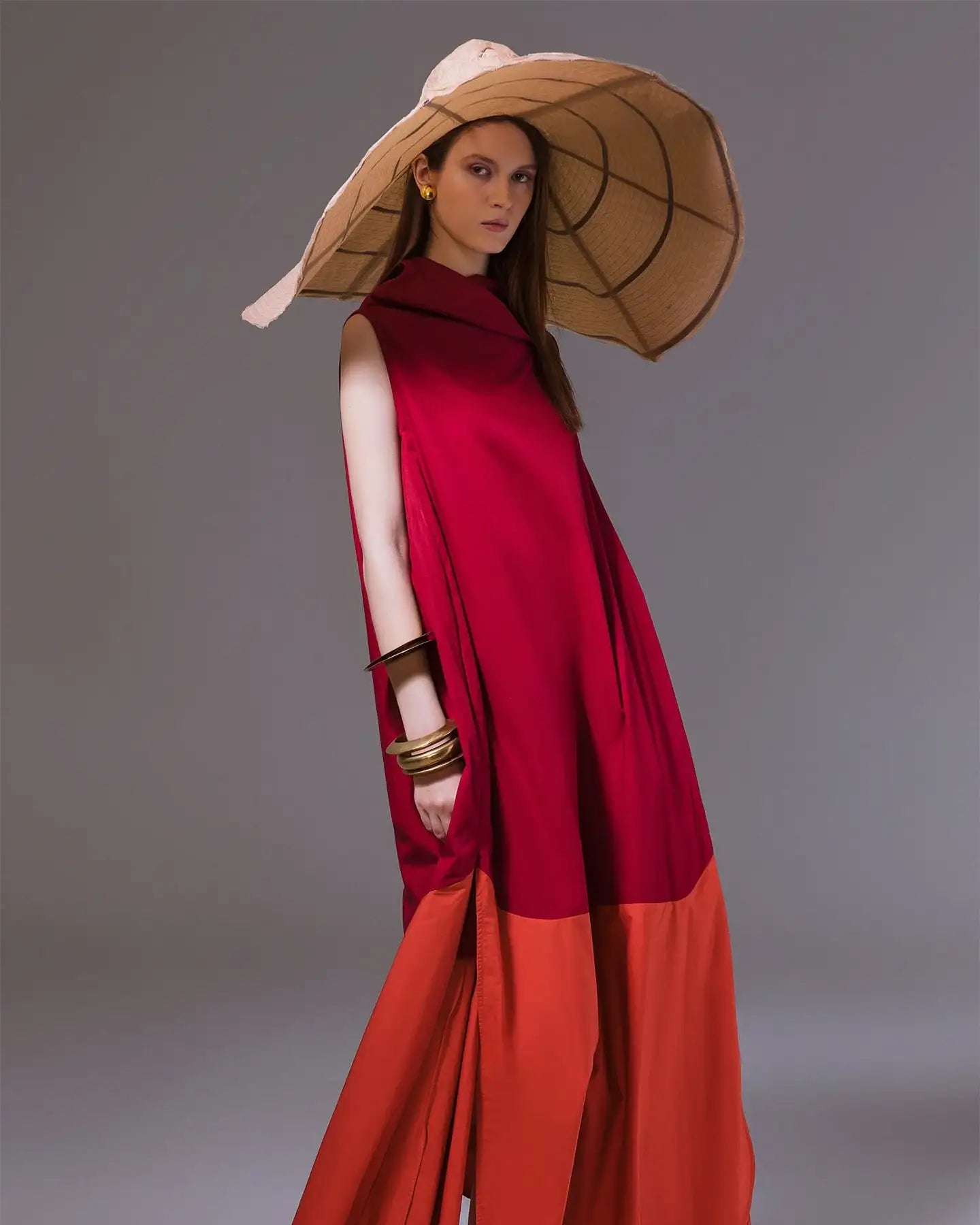 Woman in a red and orange sleeveless maxi dress with a wide brim straw hat and gold bangles