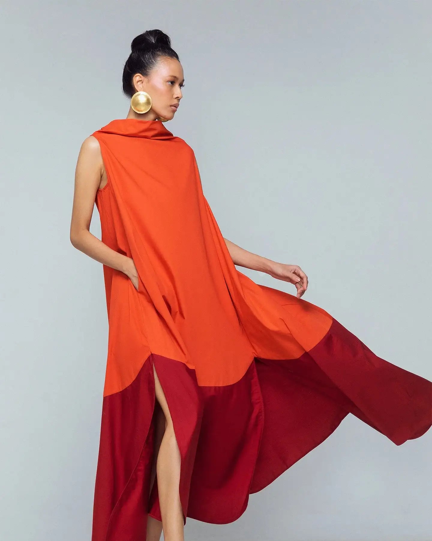 Woman wearing sleeveless orange and red colorblock maxi dress with gold statement earrings