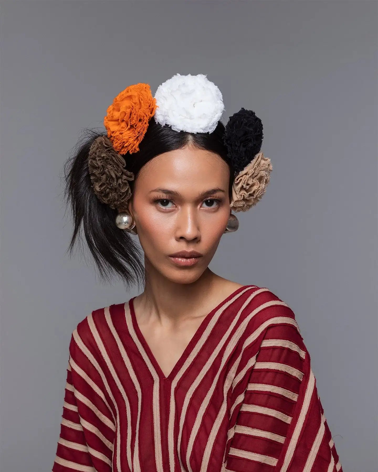 Woman in striped red and beige top with large fabric hair accessories in multiple colors