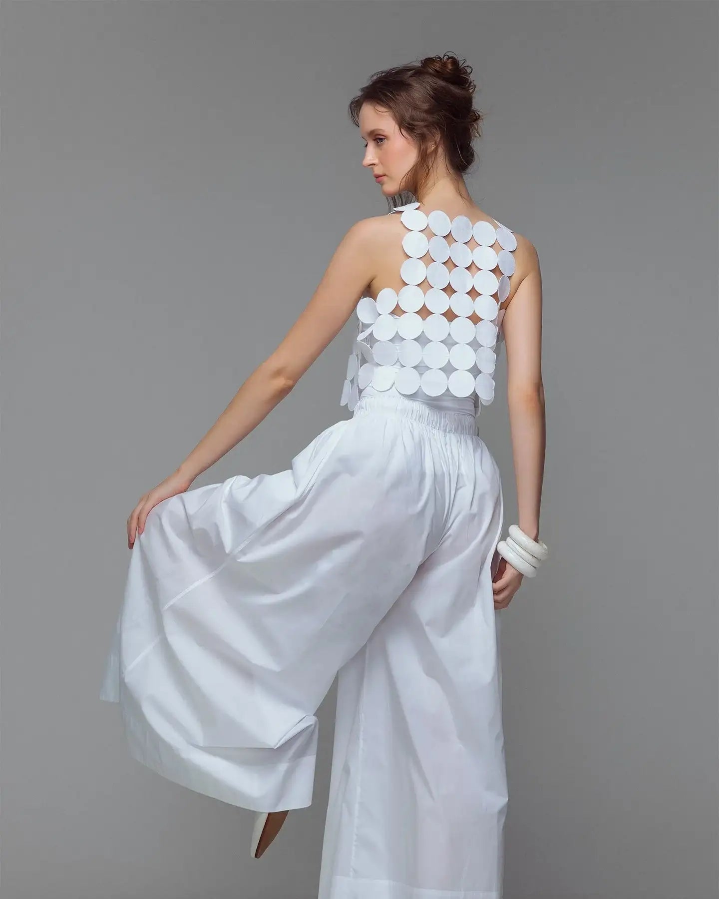 Woman in modern white sleeveless geometric top and wide-leg pants, minimalist fashion look