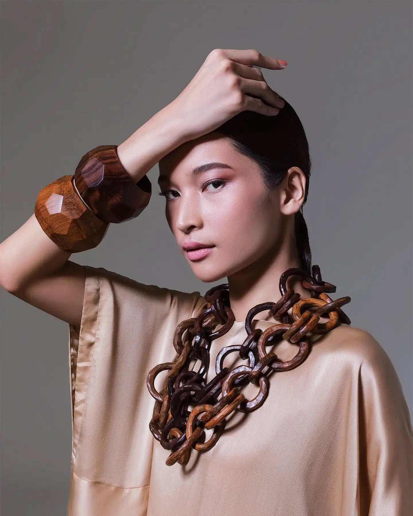 Woman in beige satin top wearing chunky wooden chain necklace and faceted wooden bangles
