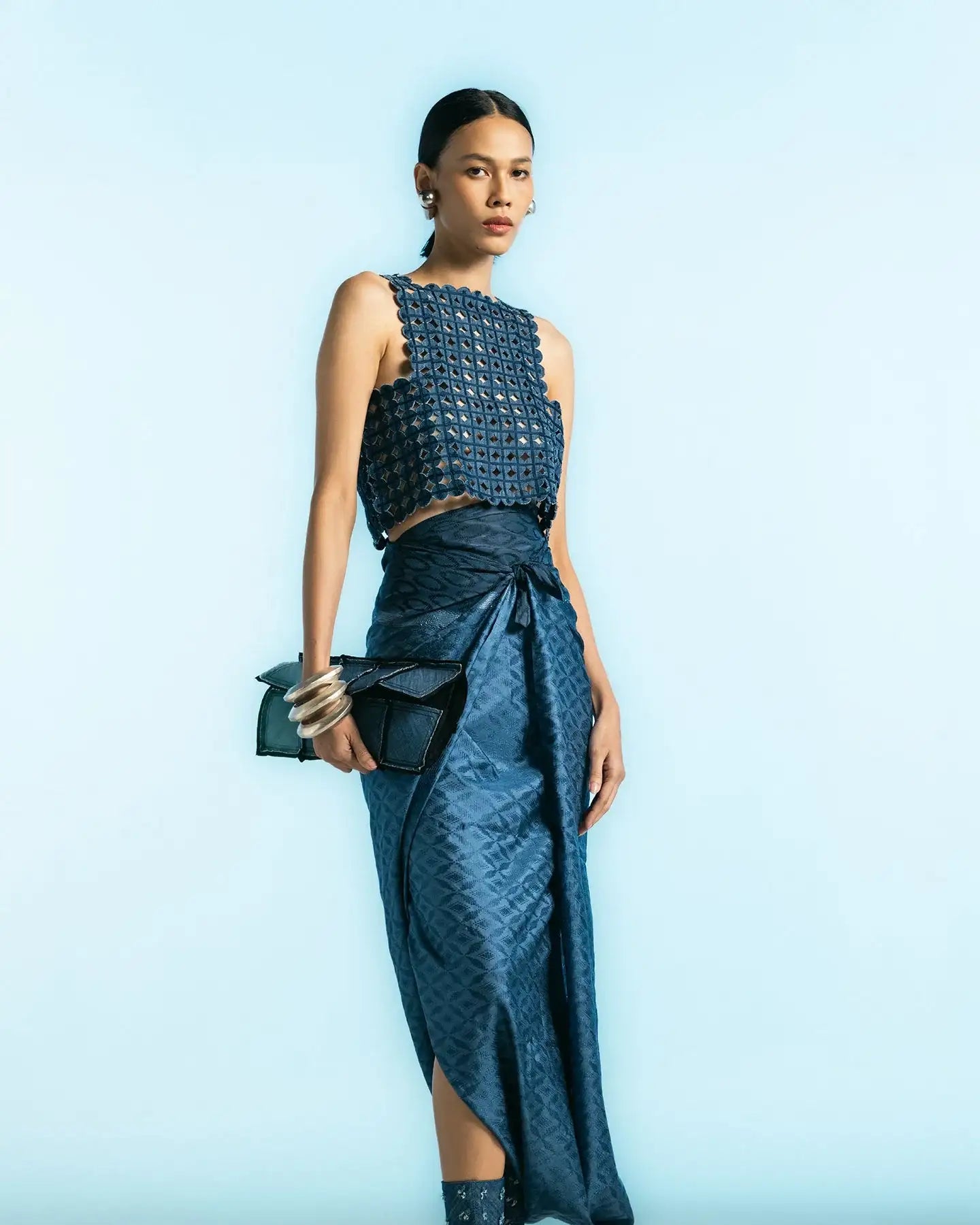 Woman wearing modern blue textured top, wrap skirt, patterned boots, holding black clutch