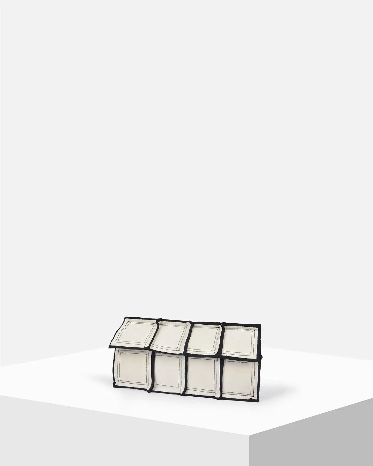 Geometric rectangular white clutch bag with black trim on a minimalist display pedestal