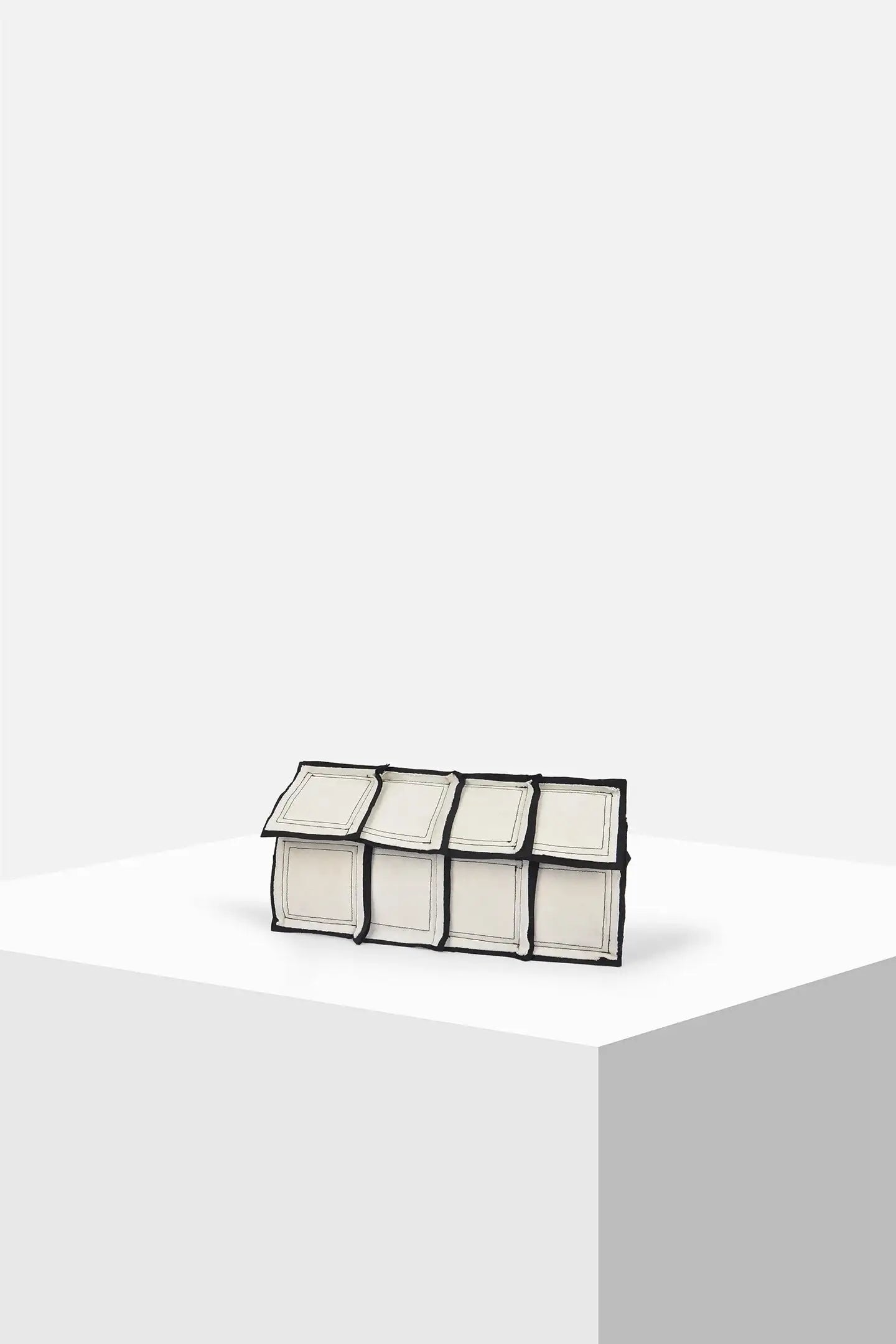 Geometric rectangular white clutch bag with black trim on a minimalist display pedestal