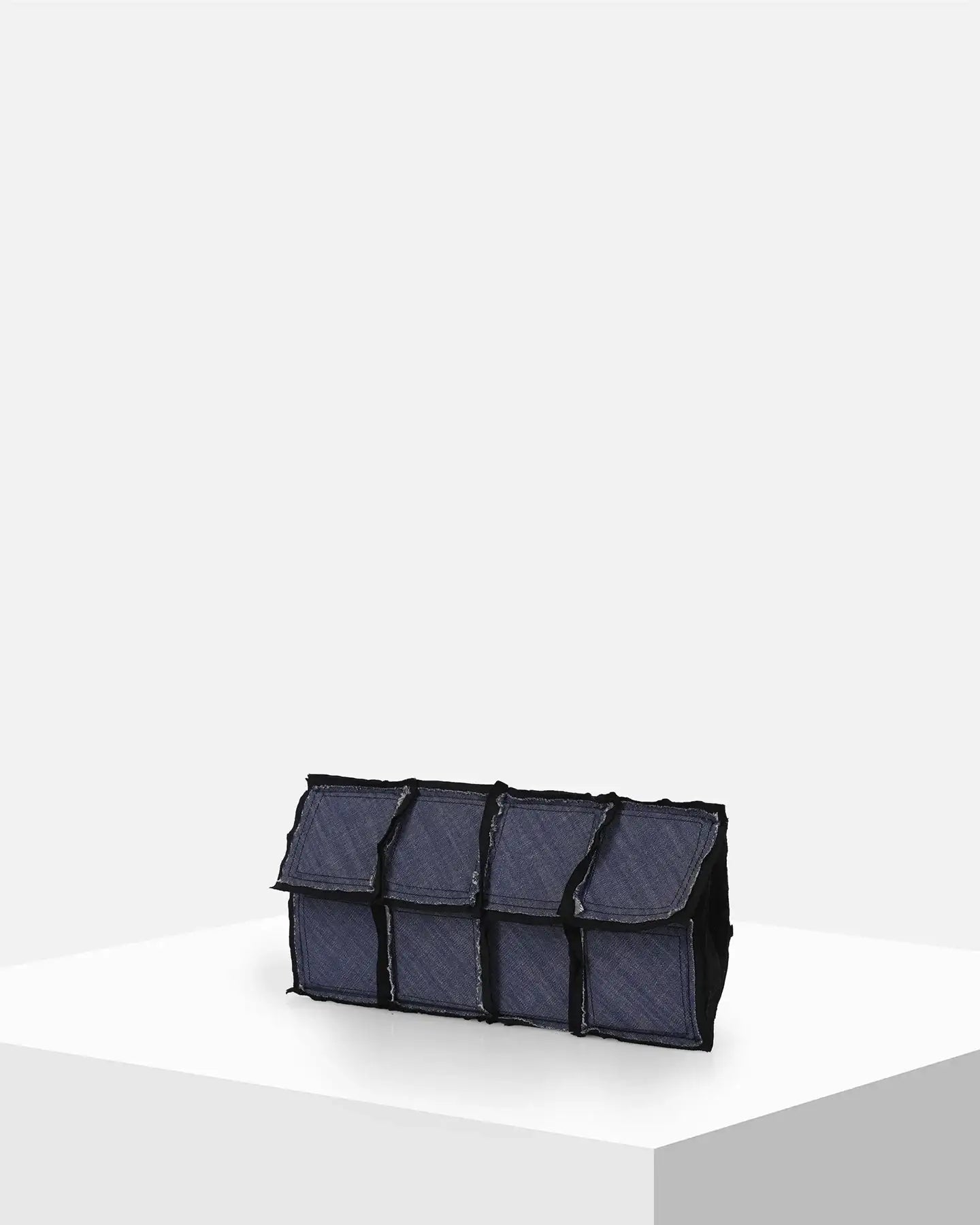 Rectangular blue denim clutch bag with patchwork design on white display pedestal