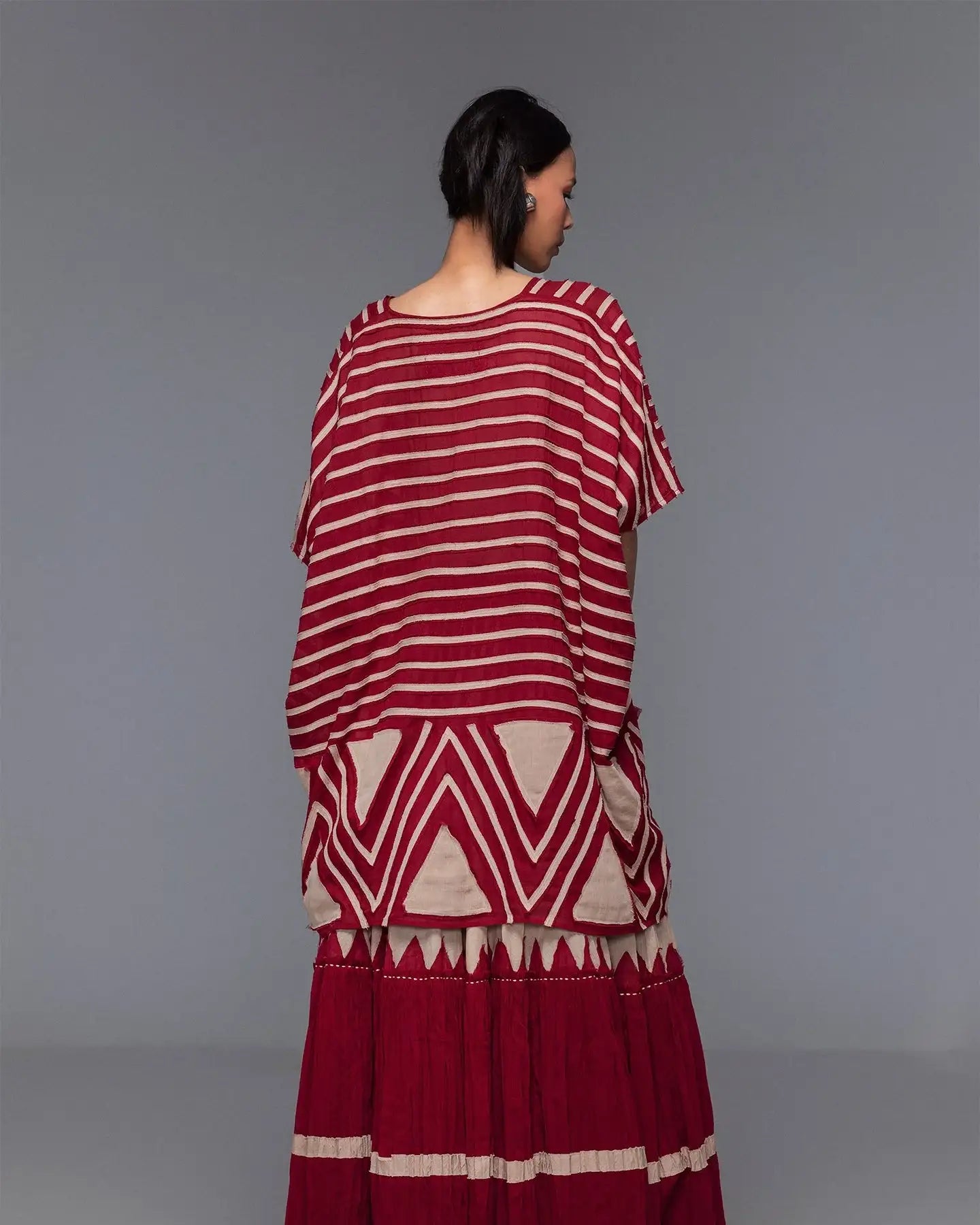 Woman wearing a loose red and beige striped and geometric maxi dress, back view