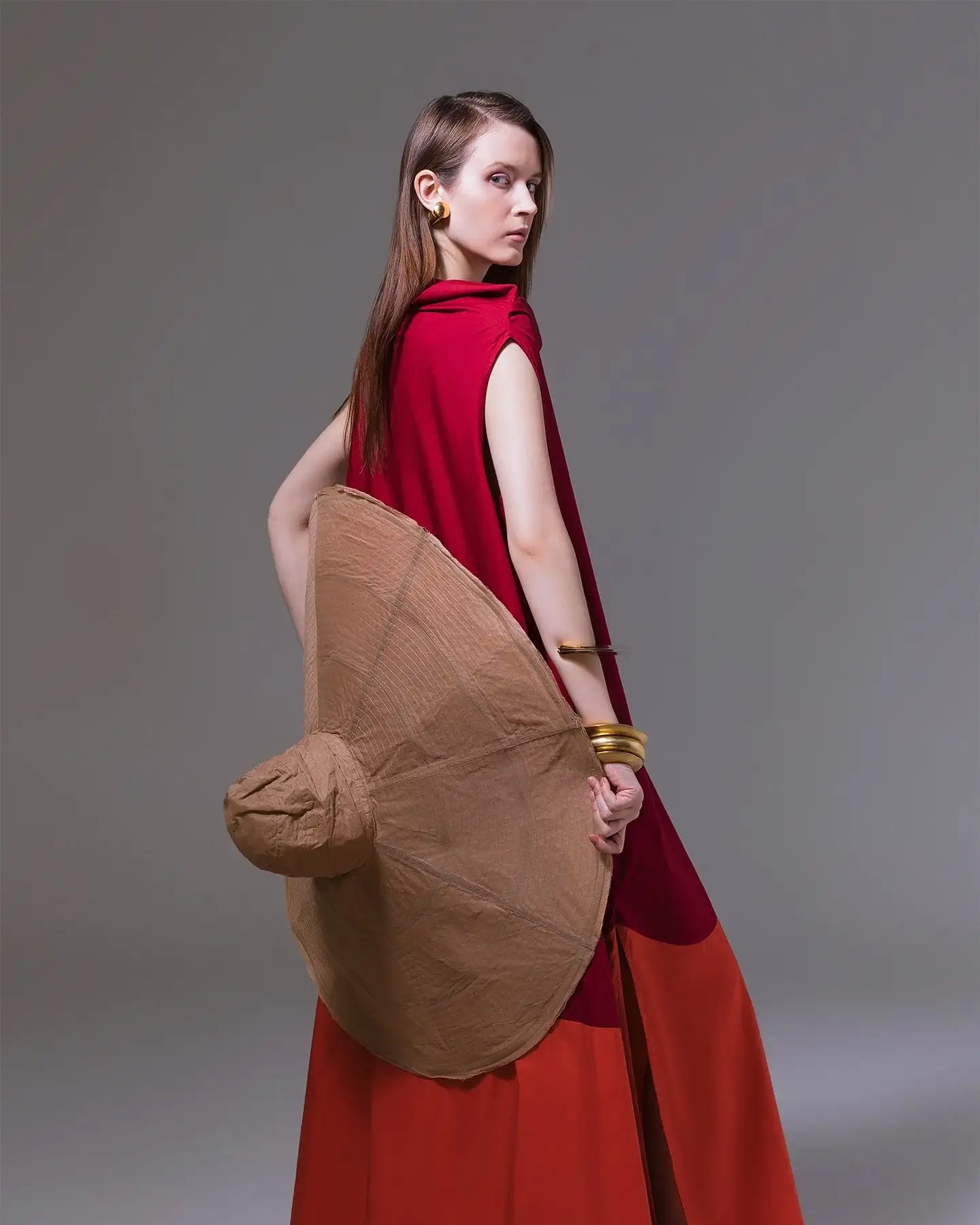 Woman in red and orange modern dress with oversized brown hat and gold accessories