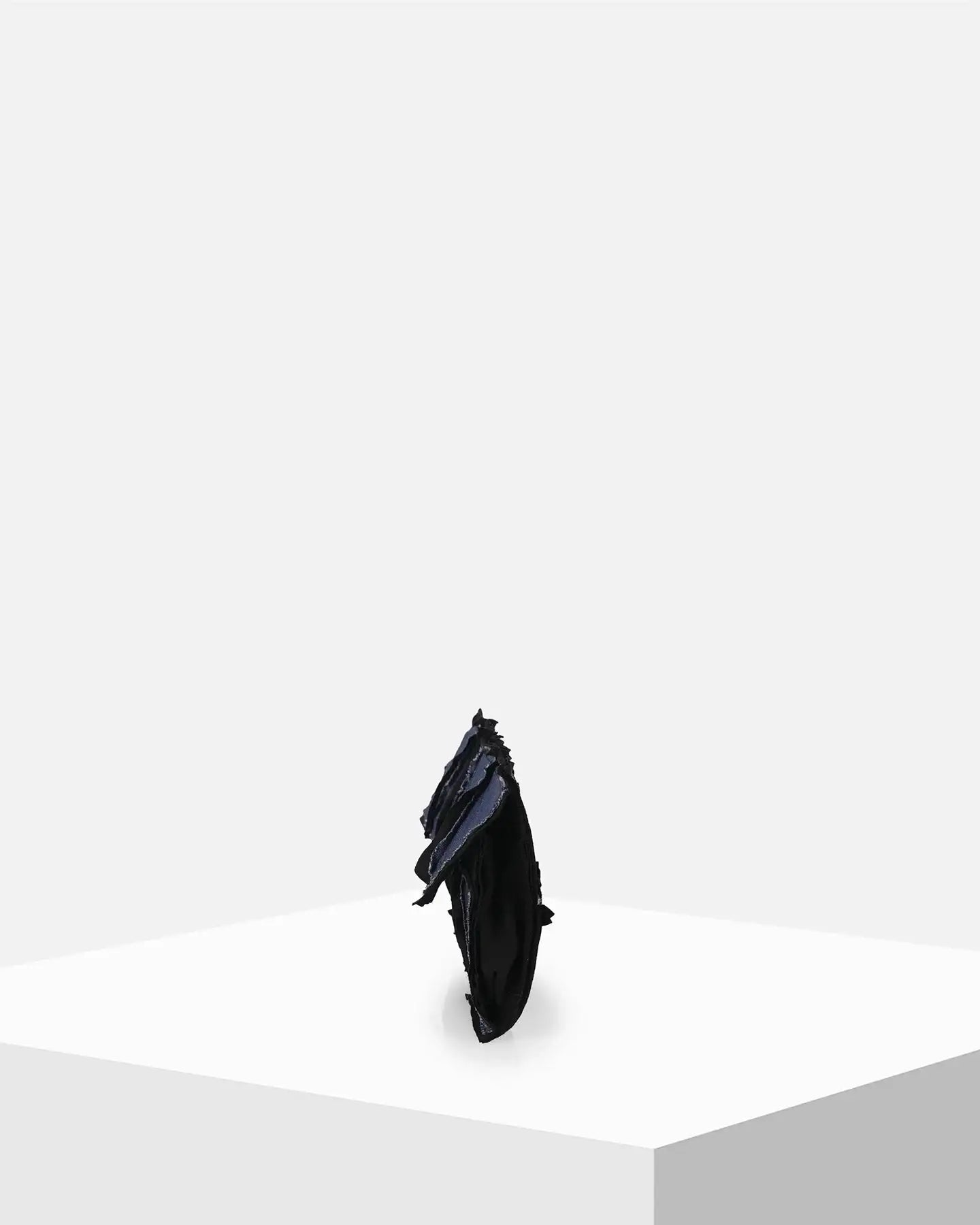 Black sculptural accessory with layered textures on white display pedestal
