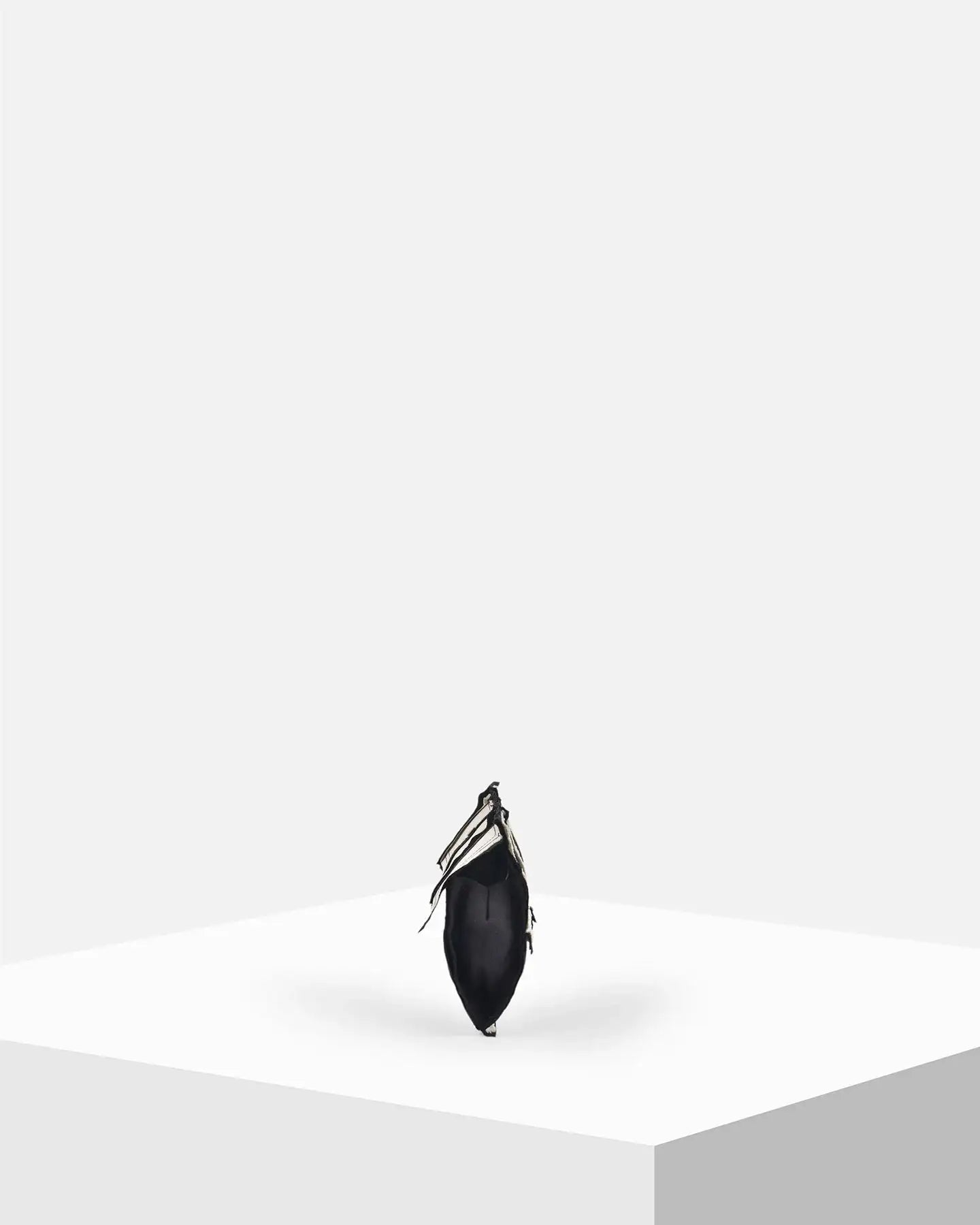 Minimalist black handbag with fringe detailing on white geometric display stand