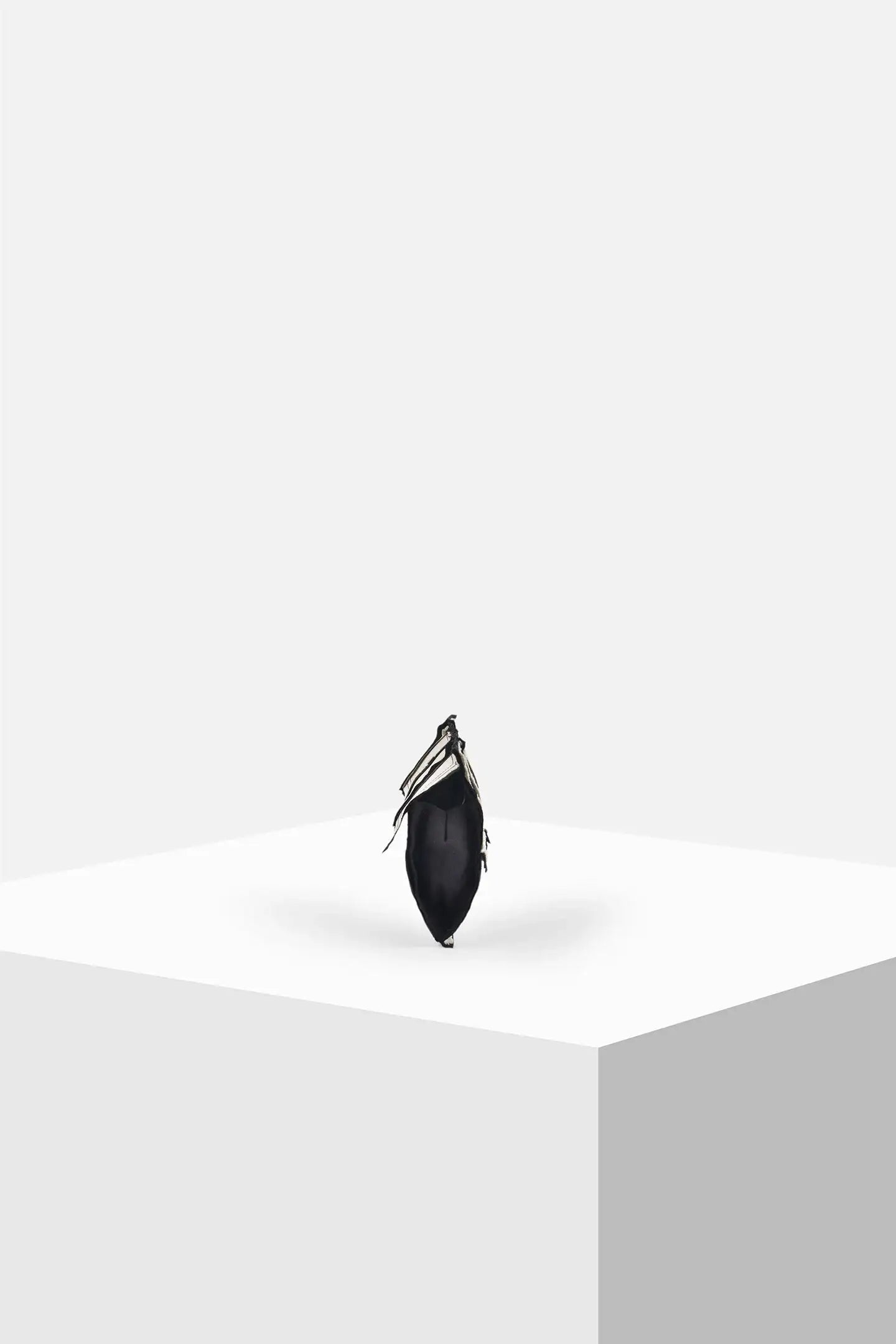 Minimalist black handbag with fringe detailing on white geometric display stand