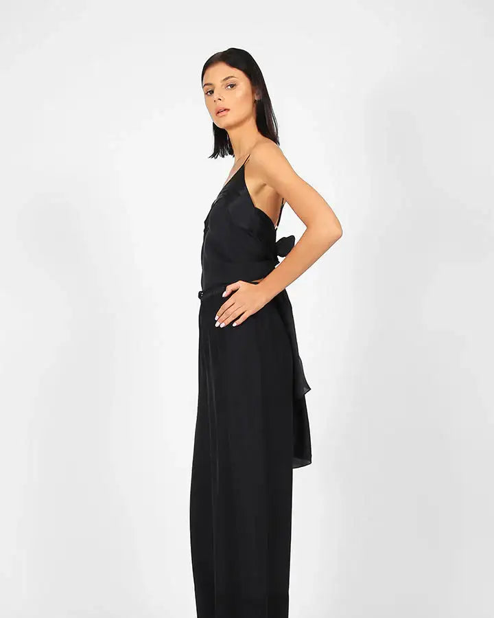 Woman posing in sleeveless black jumpsuit with wide-leg pants against white background