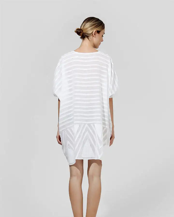 Back view of woman wearing loose white sheer striped dress, minimalist studio setting