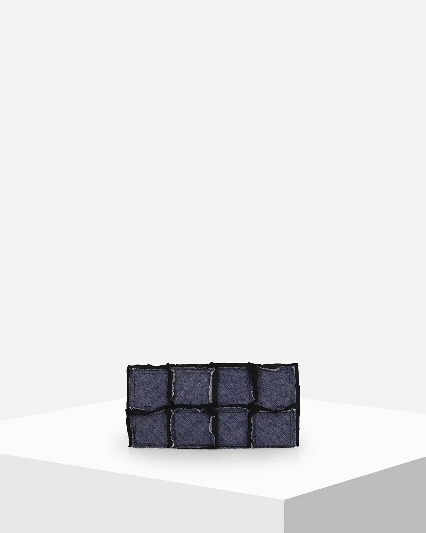 Dark blue denim patchwork clutch bag on minimal white display pedestal