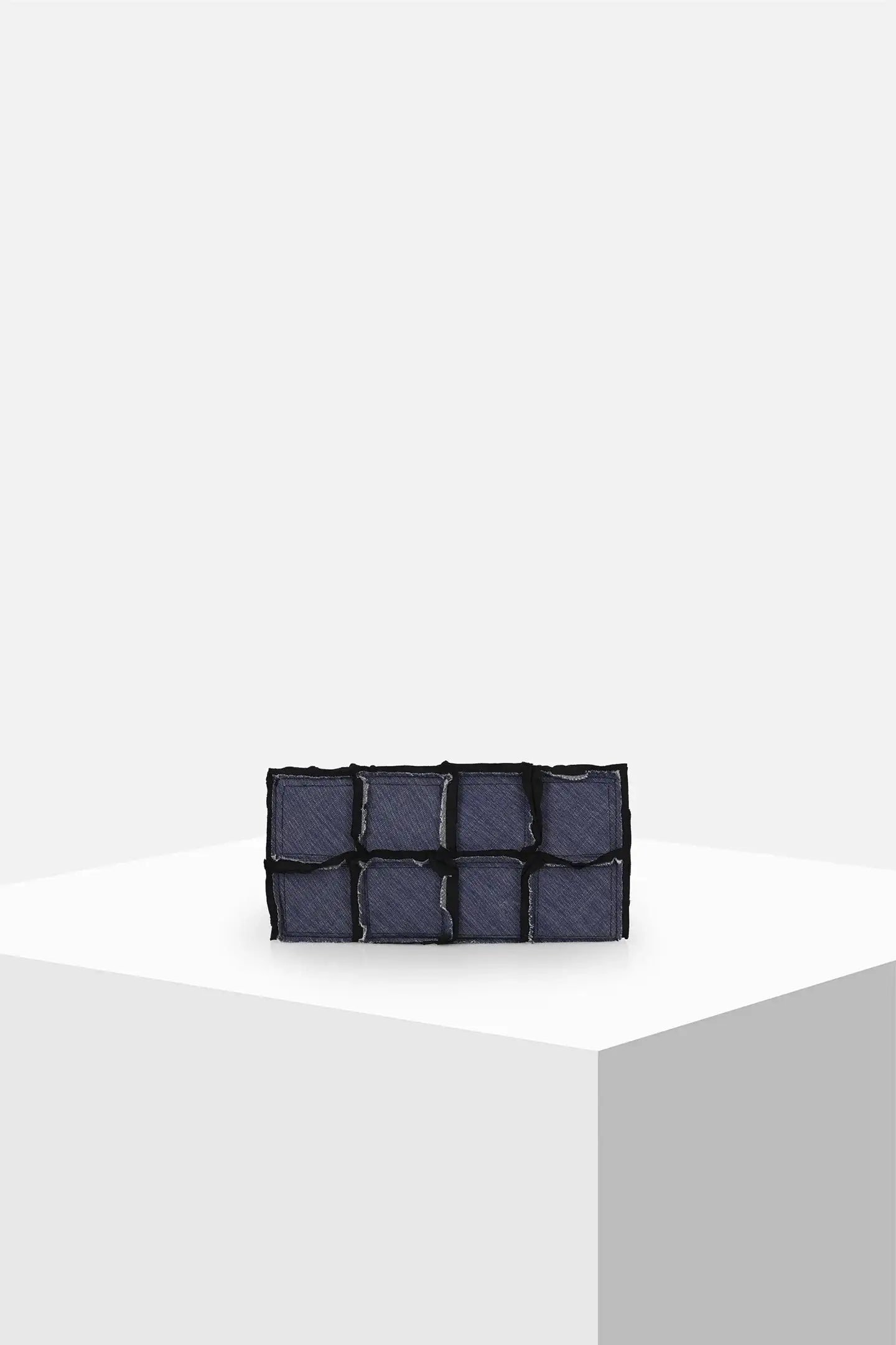 Dark blue denim patchwork clutch bag on minimal white display pedestal