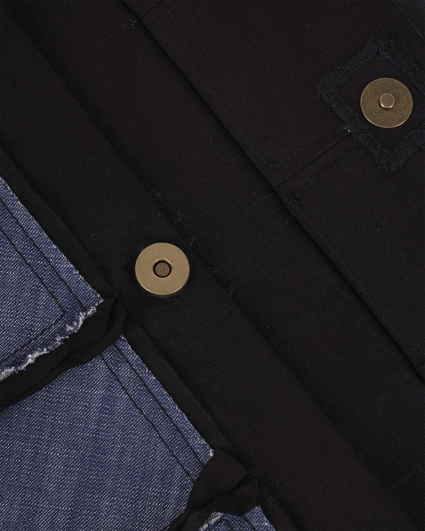 Close-up of blue denim and black fabric with metal snap button details on apparel