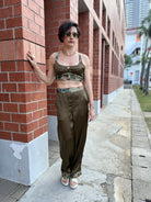 Woman in olive green crop top and pants with camouflage accents, standing by brick wall outdoors