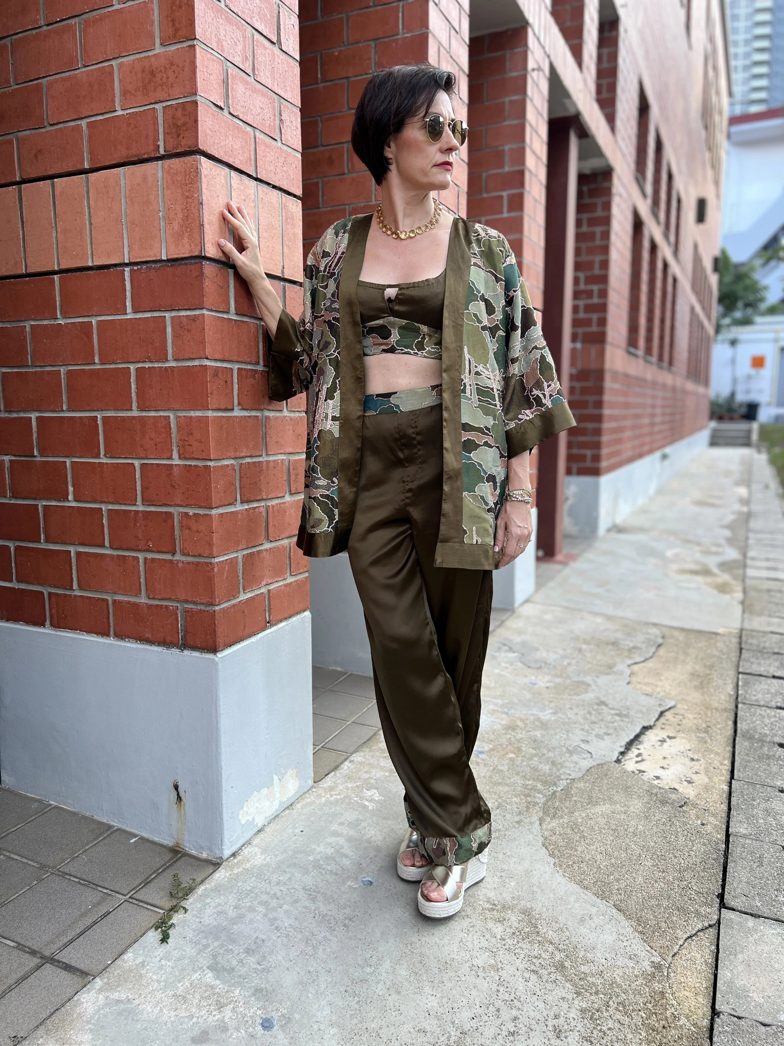 Woman in chic olive green printed kimono set, gold necklace, sunglasses, city background