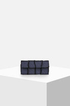 Dark denim patchwork clutch bag with textured pockets on a minimalist white pedestal