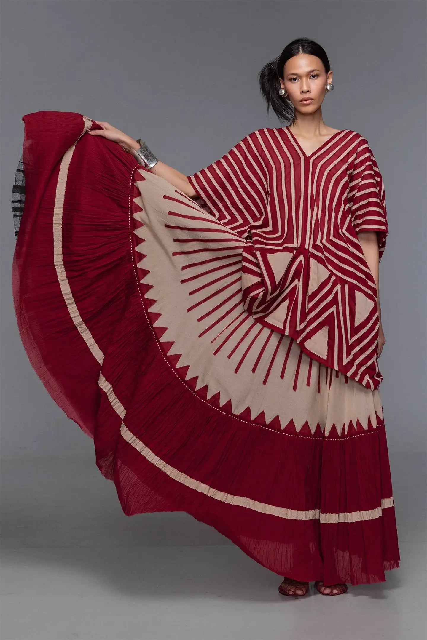Woman wearing modern red and beige geometric-patterned dress with flowy skirt, studio backdrop