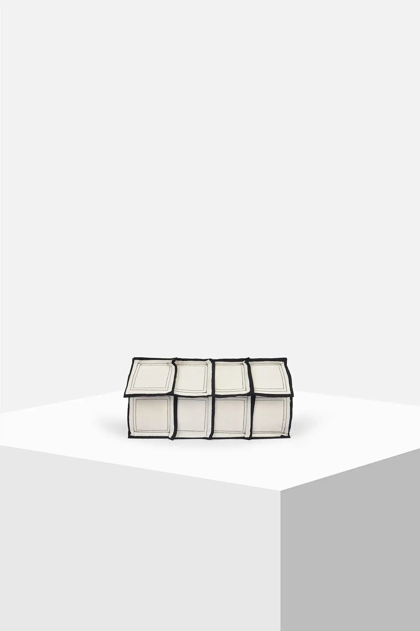 Geometric white and black clutch bag with paneled design on a minimalist display pedestal.
