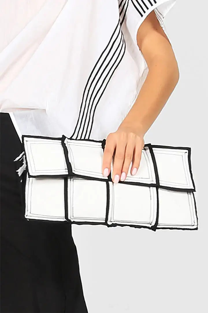 Woman holding a modern white geometric clutch bag with black trim, stylish fashion accessory