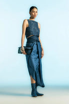 Woman wearing modern blue textured top, wrap skirt, patterned boots, holding black clutch