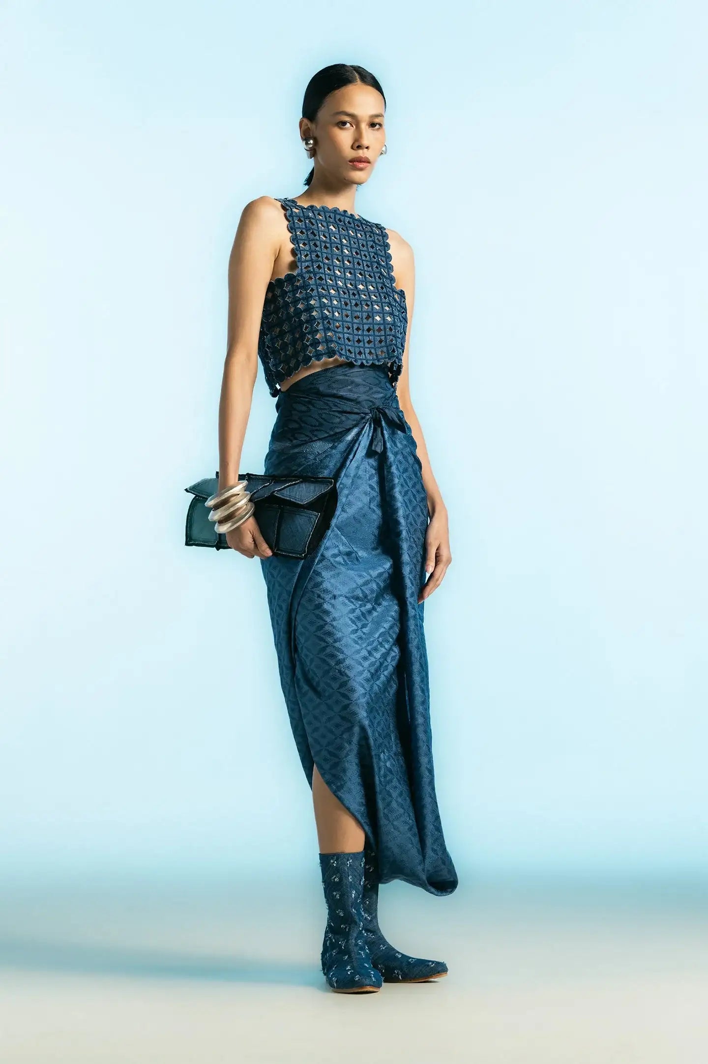 Woman wearing modern blue textured top, wrap skirt, patterned boots, holding black clutch