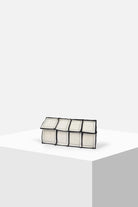 Geometric rectangular white clutch bag with black trim on a minimalist display pedestal