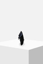 Black sculptural accessory with layered textures on white display pedestal