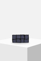 Dark blue denim patchwork clutch bag on minimal white display pedestal