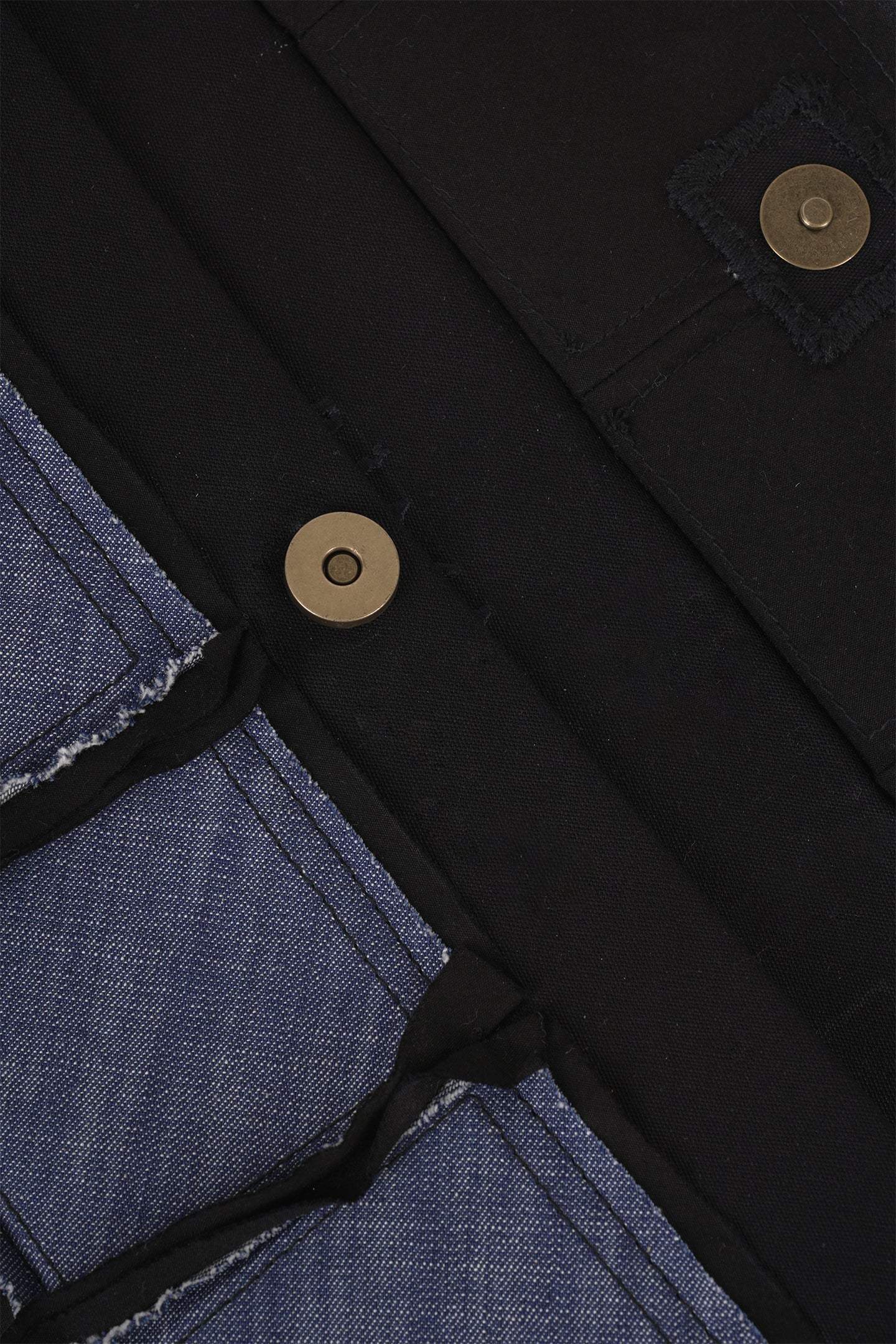 Close-up of blue denim and black fabric with metal snap button details on apparel